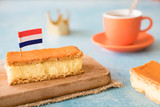 Fototapeta Sawanna - Orange tompouce, traditional Dutch treat with pudding and frosting on national holiday Kings Day (April 27th), in The Netherlands. With cup of coffee, crown and Dutch flag