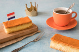 Fototapeta Sawanna - Orange tompouce, traditional Dutch treat with pudding and frosting on national holiday Kings Day (April 27th), in The Netherlands. With cup of tea, crown and Dutch flag