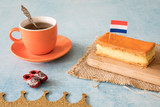 Fototapeta Sawanna - Orange tompouce, traditional Dutch treat with pudding and frosting on national holiday Kings Day (April 27th), in The Netherlands. With cup of coffee, wooden shoes and Dutch flag