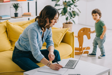 Wall Mural - kid looking how mother working with laptop in living room