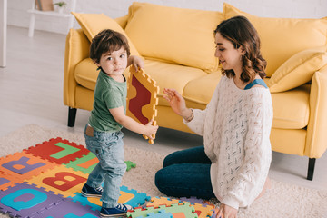 Wall Mural - Smiling mother and kid playing with alphabet puzzle mat