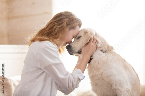 Fotografía Young pretty woman in casual clothes hugging her beloved big white dog sitting on the sofa in the living room of her cozy country house