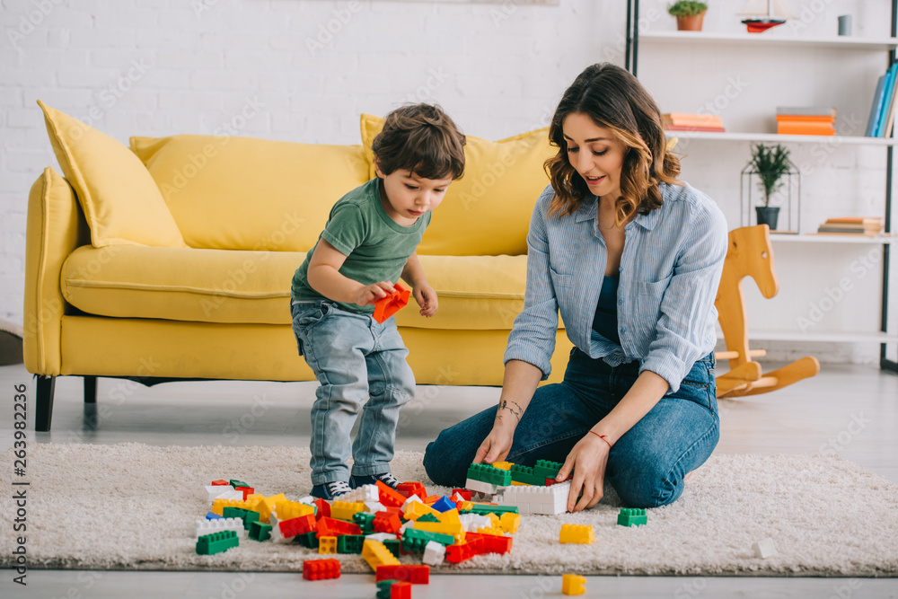 Mother and son playing with lego on carpet in living room - obrazy, fototapety, plakaty 
