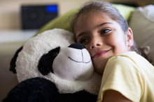 Little Girl Lying On Couch At Home Cuddling With Teddy Panda Bear