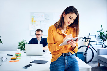 Businesswoman using tablet in office with colleague in background