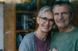 © Westend61 - Portrait of happy senior couple behind windowpane
