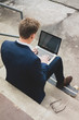 © Westend61 - Young businessman with skateboard sitting outdoors on stairs using laptop