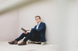 © Westend61 - Young businessman with skateboard sitting outdoors using tablet