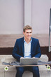 © Westend61 - Smiling young businessman with skateboard sitting outdoors on stairs using laptop