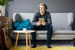 © Westend61 - Smiling young man with guitar, tablet and headphones sitting on couch