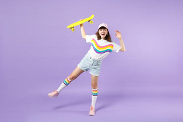 Wall Mural - Portrait of cheerful teen girl in vivid clothes having fun holding yellow skateboard isolated on violet pastel wall background in studio. People sincere emotions lifestyle concept. Mock up copy space.