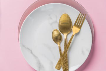 Wall Mural - marble plate, gold knife,fork and spoon on pink background.dishes and Cutlery, plate with spoons and fork.Art decor.dinner, romantic love food and love cooking concept.Copy space