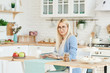 © oes - Freelance concept. Beautiful business woman in casual clothes and glasses is examining documents and smiling while working with a laptop in kitchen. Working at home