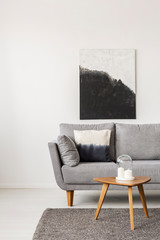 Wall Mural - Abstract black and white painting on empty white wall with wooden coffee table with candles and grey sofa with pillow