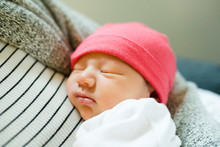 Sleeping Newborn Baby Girl Being Held In Mother's Arms Wearing Hat