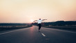 Man with arms outstretched riding a skateboard on the motorway road toward the setting sun in the background. The background is slightly blurred, focus on a skateboarder in the foreground.