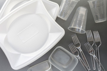 No use symbol in red forbidden sign with plastic dishes around disposable paper dishes and a wooden fork and knife on gray background. Environmental concept. Ban single use plastic.