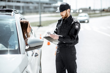 Wall Mural - Policeman checking documents of a young female driver standing near the car on the roadside in the city