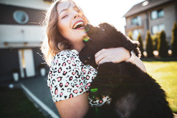 The blonde girl is playing with the cute baby newfoundland dog on a sunny beautiful day in the garden