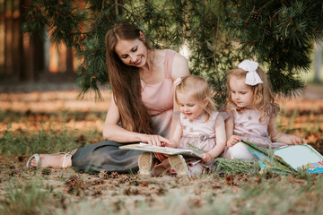 Outdoor portrait of two little girl is reading a book on the grass with mother. She has a look of pleasure and she looked very relaxed in her mother's arms.