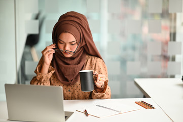 Wall Mural - Islam woman working with laptop and holding a coffee mug and glasses.