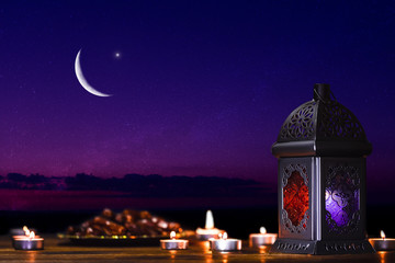 Ornamental dark Moroccan, Arabic lantern and dates on on an old wooden table with the night sky and the Crescent moon and the stars behind. Greeting card for Muslim community holy month Ramadan Kareem