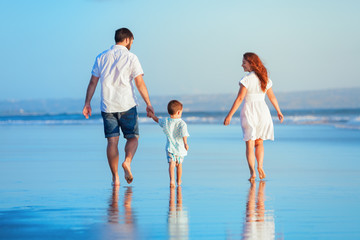 Wall Mural - Happy family - young father, mother, baby son strolling together, child run with fun by water pool along sunset sea surf on tropical beach. Travel lifestyle, people walking with kid on summer vacation