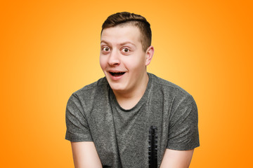 Wall Mural - Portrait of a surprised, funny positive guy on a bright orange background in the studio.