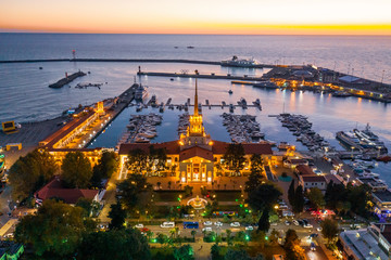 Wall Mural - Aerial photography with quadrocopter. Sea port of Sochi with a bird's eye view. Evening illumination of the building. Yachts and boats are in the port. Resort town. Landmark. 