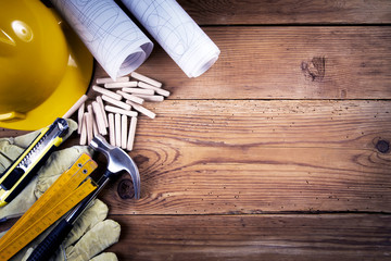 hammer, protective gloves, folding ruler, model knife, blueprint, wooden dowels  and yellow safety helmet on wooden background