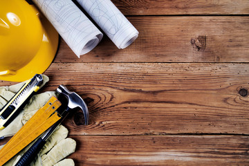 hammer, protective gloves, folding ruler, model knife, blueprint and yellow safety helmet on wooden background