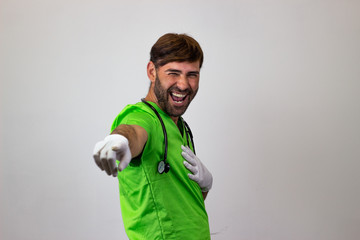 Wall Mural - Portrait of male veterinary doctor in green uniform with brown hair pointing while laughing, their back facing the camera and looking at the camera. Isolated on white background.