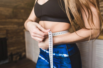 Sticker - Beautiful young woman in sportswear measures the measured flight waist circumference. Sport, diet and weight loss