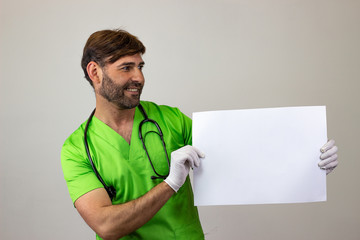 Wall Mural - Portrait of male veterinary doctor in green uniform with brown hair holding a blank sign, facing forwards and looking at the side. Isolated on white background.