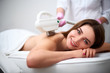 © artiemedvedev - Young pretty smiling woman back laser epilation in beauty salon. Cosmetologist doing depilation treatment with elos device. Beautician hands in gloves holding hair removal cosmetology ipl hardware