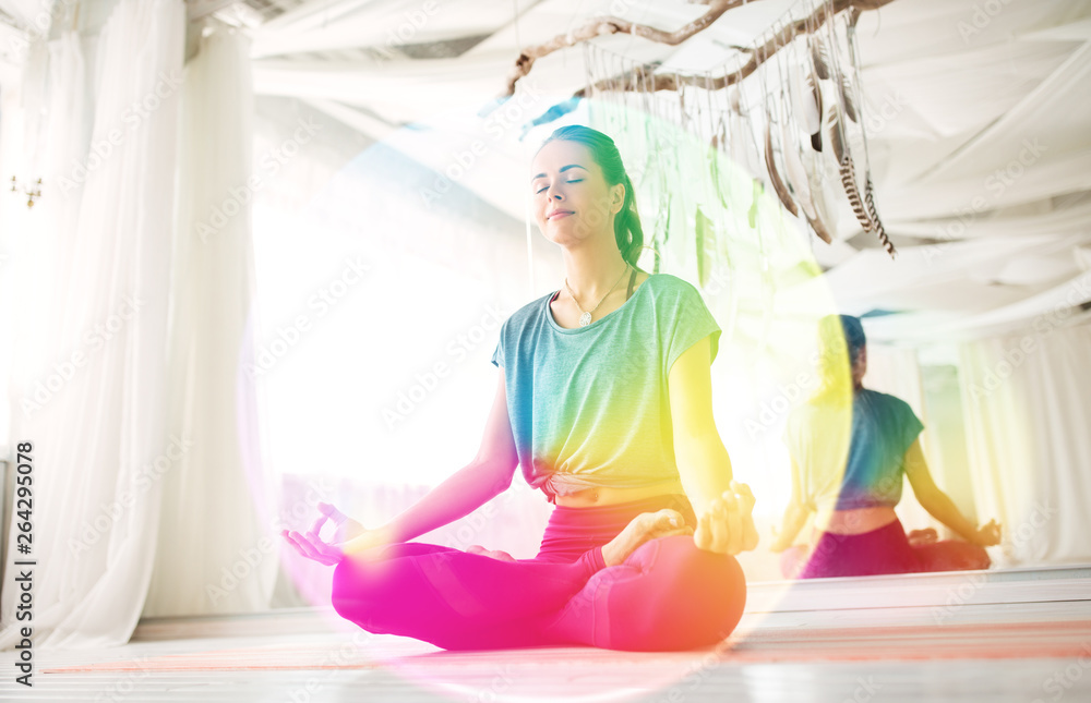 mindfulness, spirituality and healthy lifestyle concept - woman meditating in lotus pose at yoga studio over rainbow aura - obrazy, fototapety, plakaty 