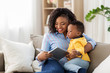 © Syda Productions - childhood, kids and people concept - happy african american mother with book and her baby son at home
