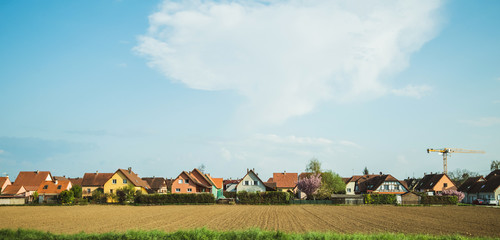 Beautiful clean wealthy French village of Benfeld with multiple houses, construction crane large area of plowed fields and clear blue sky with some clouds