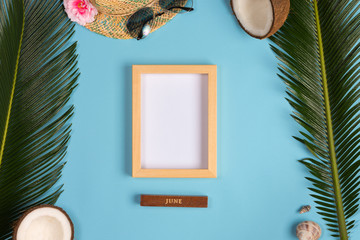 Stylish summer composition with photo frame, green leaves, hat and sunglasses on a blue pastel background. Artwork mockup with copy space