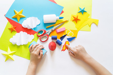 Wall Mural - hands of the child make a paper craft rocket. Cosmos clouds and stars colored paper. The creative process
