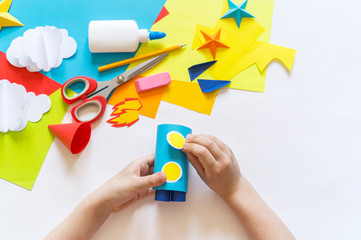 Wall Mural - hands of the child make a paper craft rocket. Cosmos clouds and stars colored paper. The creative process