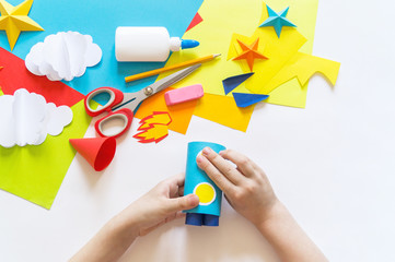 Wall Mural - hands of the child make a paper craft rocket. Cosmos clouds and stars colored paper. The creative process