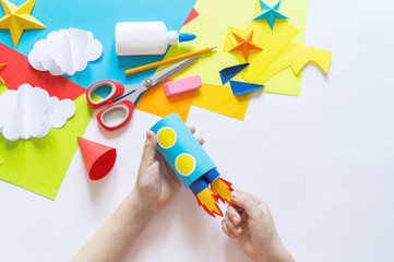 Wall Mural - hands of the child make a paper craft rocket. Cosmos clouds and stars colored paper. The creative process