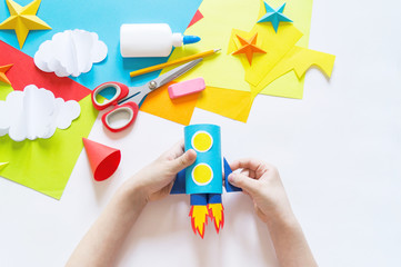 Wall Mural - hands of the child make a paper craft rocket. Cosmos clouds and stars colored paper. The creative process