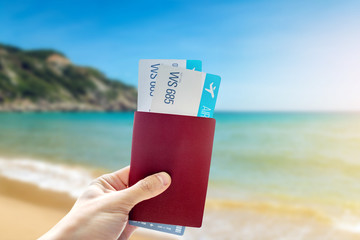 Hand holding a passport and two air tickets on a blue background of the sea. Travel and vacation in exotic places