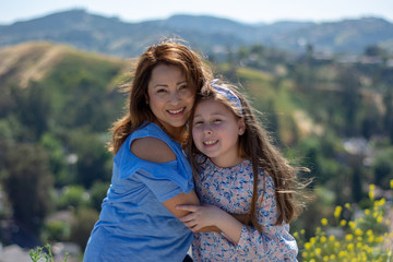 Latina Mother and Daughter Smiling and laughing on a hill in front of yellow flowers