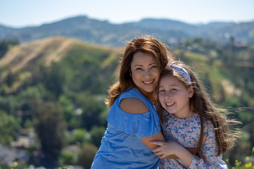 Latina Mother and Daughter Smiling and laughing on a hill in front of yellow flowers