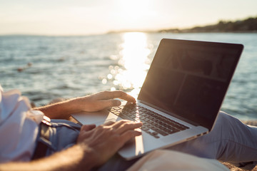 Senior man working on his laptop lying on deck chair on the beach during sunset