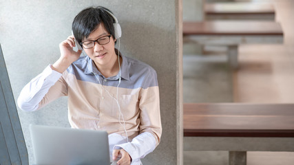 Wall Mural - Young Asian man university student enjoy listening to music with headphones using laptop computer in the college. Education and entertainment media technology concept