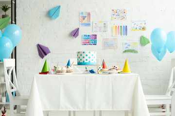 festive cake and party caps on table in room decorated for birthday party with air balloons